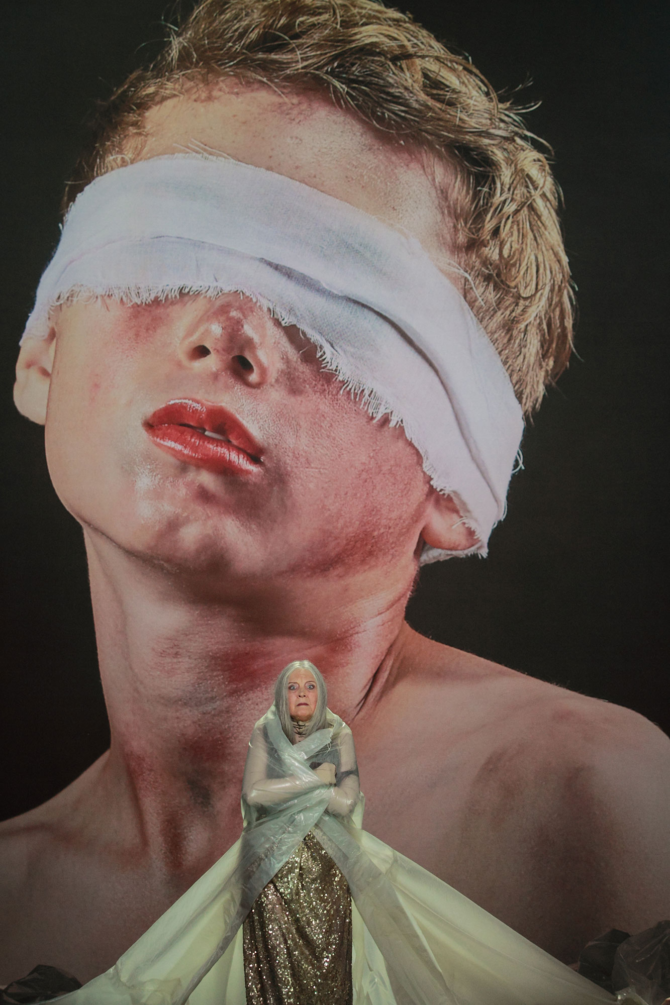 Scene with woman standing in front of photo of woman with bandaged eyes