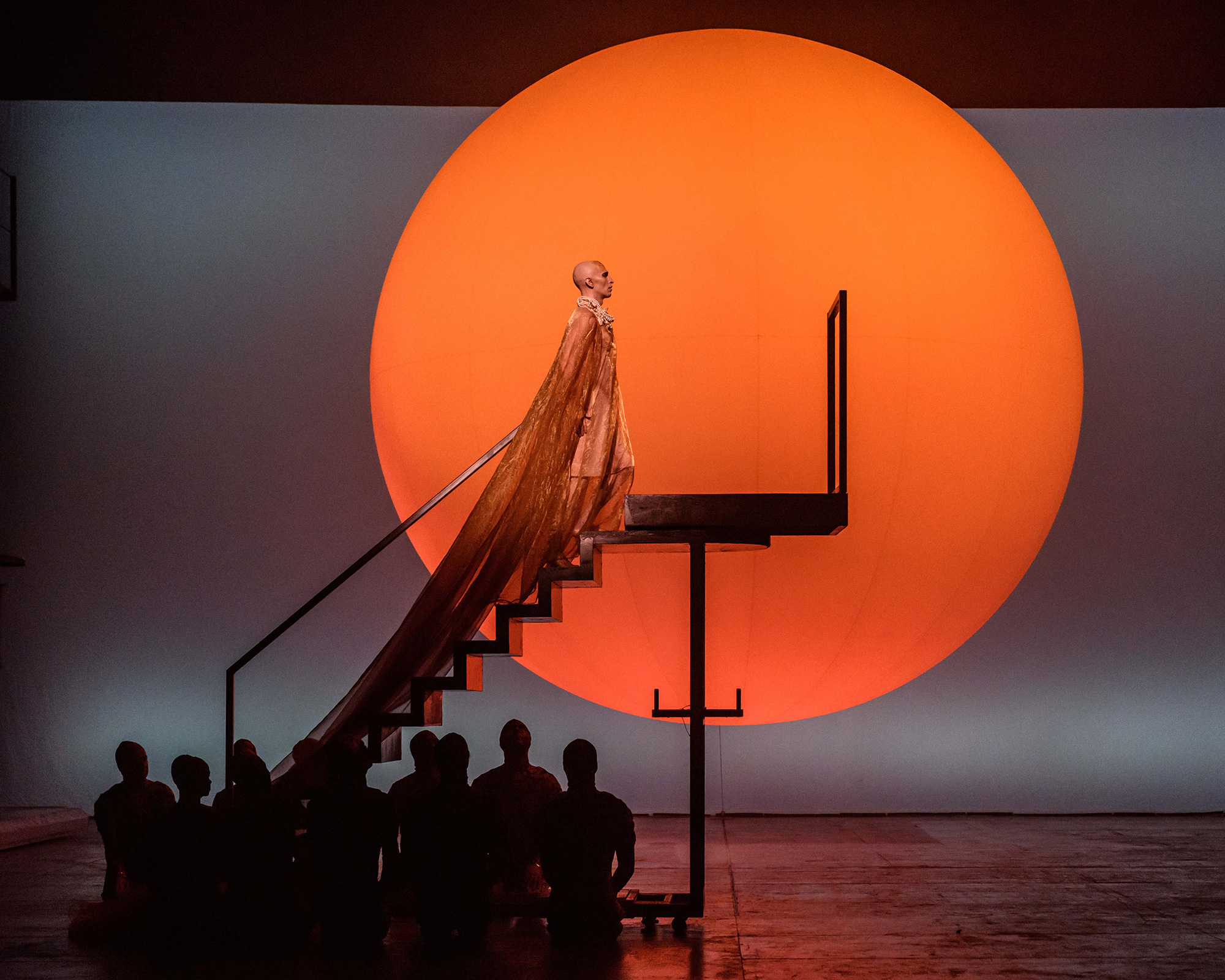 Akhnaten walking up steps with sunset in background