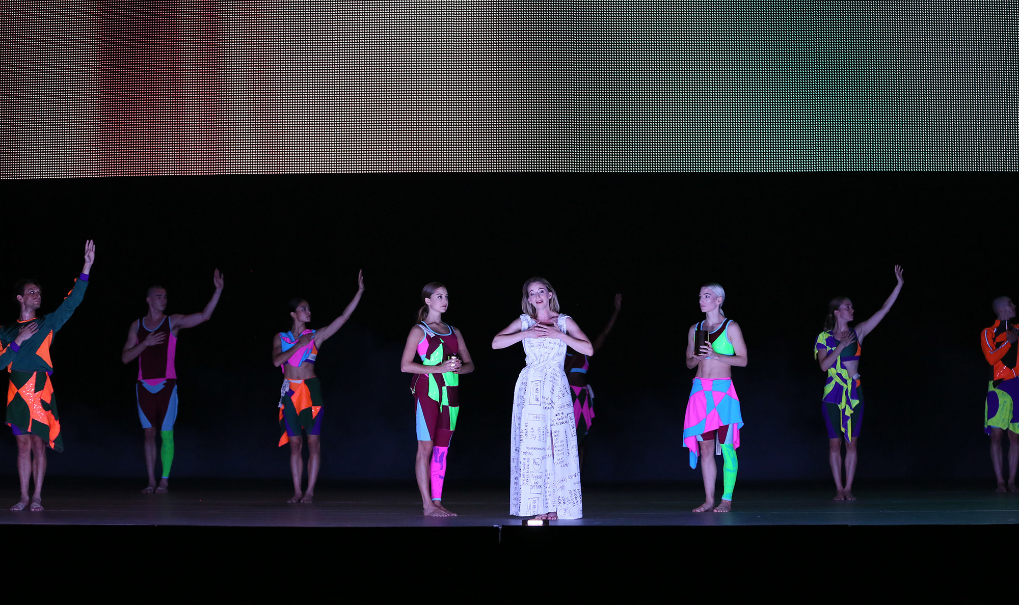 Dancers on stage with woman in a white dress in the centre.