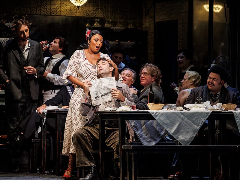 Woman singing stanidng by a dinner table with men eating