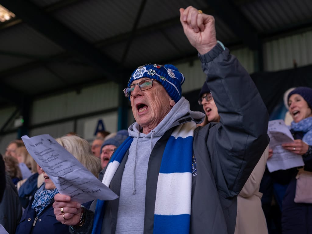 Man with blue and white scarf singing with his arm in the air