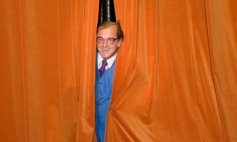 Man peeking through orange theatre curtains